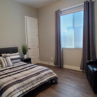 A modern, minimalist bedroom featuring striped bedding and a large window with curtains.