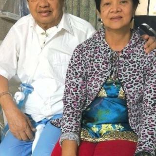 An older couple sitting together indoors, dressed in casual clothing.