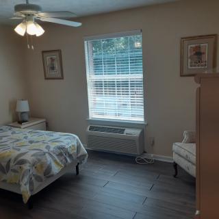 A cozy bedroom with a bed, dresser, and a chair near a window with blinds.