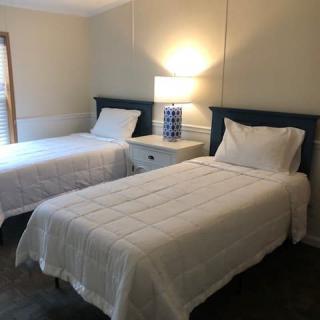 A minimalist bedroom with twin beds and a central nightstand with a lamp.