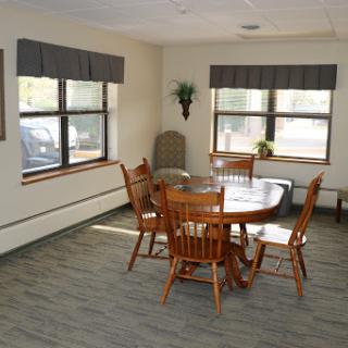 A cozy dining area with wooden furniture and ample natural light from large windows.
