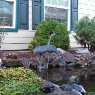 A garden with a pond and a metal bird sculpture in front of a house.