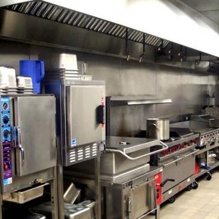 A clean and well-organized commercial kitchen equipped with industrial cooking appliances and a vent hood.