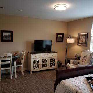 A cozy living room with a TV, table, chair, and lamp.