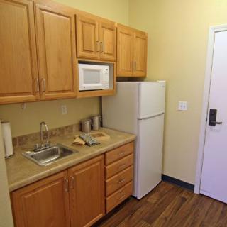 Compact kitchen space with wooden cabinets, a refrigerator, microwave, and sink.
