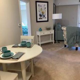 A cozy living and dining space featuring a small table set with teal dishes, a comfortable chair, and tasteful decor.