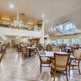 A spacious and well-lit dining area with numerous tables and chairs, featuring elegant lighting fixtures.