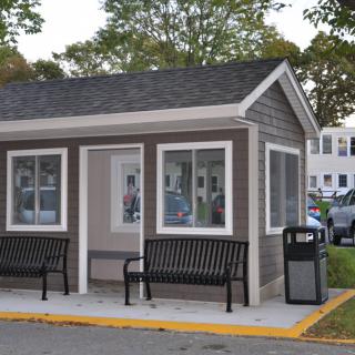 A small bus stop shelter with benches and a trash can outside, set in a suburban area.