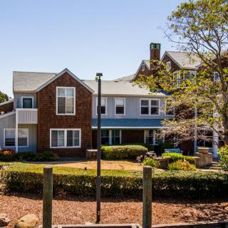 A two-story residential house with a well-maintained yard and trees under a clear blue sky.
