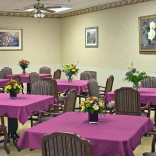 A dining room with multiple tables decorated with purple tablecloths and floral centerpieces.