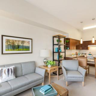 A modern open-plan living area with a cozy setup featuring a gray sofa, armchair, and a view into the kitchen.