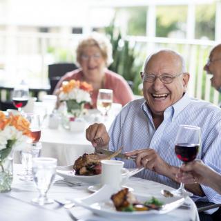 Elderly friends enjoying a meal and laughter together.
