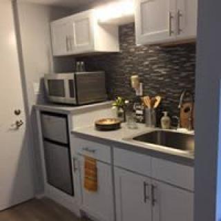 A compact modern kitchen with a sleek design, featuring a microwave, small oven, and stylish backsplash.
