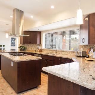 A spacious modern kitchen with a central island, wood cabinets, and granite countertops.