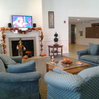 A cozy living room with blue armchairs, a fireplace adorned with autumn decorations, and a television mounted above.