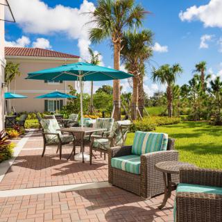 A beautifully landscaped outdoor patio with comfortable seating and umbrellas, surrounded by palm trees on a sunny day.