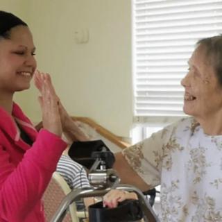 An elderly woman shares a joyful high five with a caregiver.