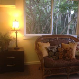 A cozy living room with a wicker sofa and cushions next to a warmly lit lamp.