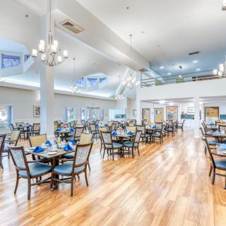 A spacious and elegantly designed dining room with multiple tables and chairs, featuring chandeliers and a polished hardwood floor.