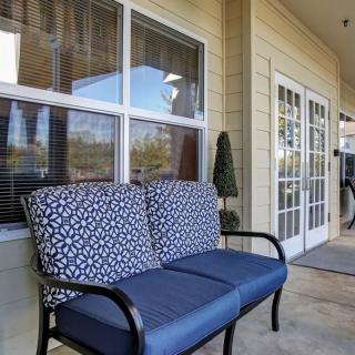 A cozy outdoor patio area featuring a cushioned bench near large windows and French doors.