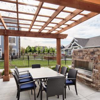 An inviting backyard patio with a pergola, featuring an outdoor dining area and a stone fireplace.