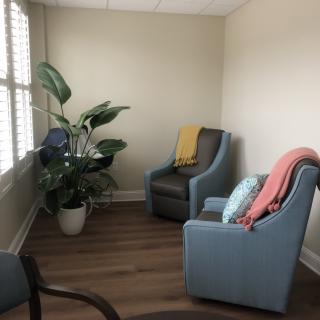 A cozy room with two chairs, a plant, and blankets near a window.