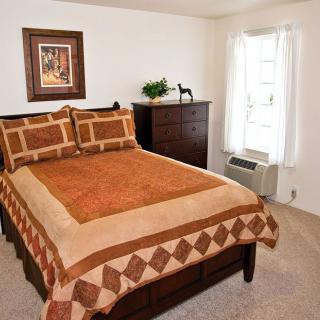 A cozy bedroom featuring a neatly made bed with a patterned quilt, a dresser, and a framed artwork above the headboard.