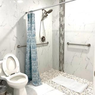 A modern bathroom with a shower area featuring a blue curtain, grab bars, and pebble flooring.