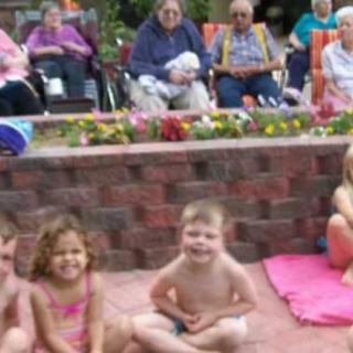 A group of children sitting in front of a low brick wall, with seniors seated in the background.