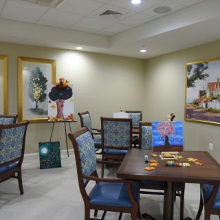A room with tables and chairs, decorated with various paintings on the walls and easels.