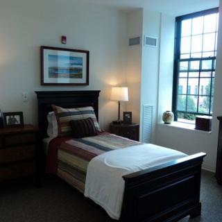 A cozy bedroom with a single bed, nightstand, and a large window letting in natural light.