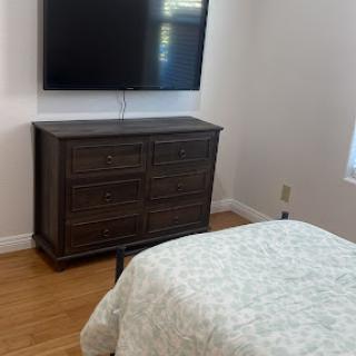 A cozy bedroom featuring a dresser and a mounted TV.