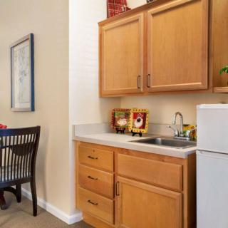 A compact kitchenette featuring wooden cabinets, a countertop with a sink, and a small refrigerator.