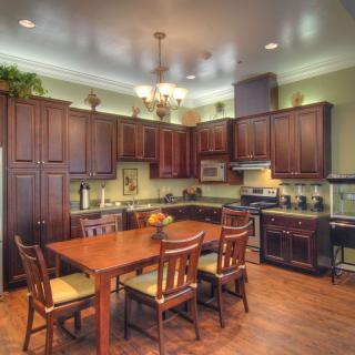 A spacious kitchen with a wooden dining table surrounded by chairs, featuring dark cabinetry and modern appliances.