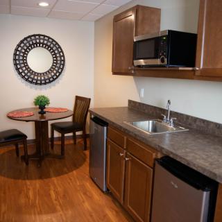 A compact, modern kitchen with wooden cabinets and a small dining area featuring a round table and chairs.
