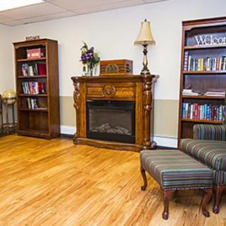 A cozy living room with a wooden fireplace, bookshelves, and an armchair on a hardwood floor.