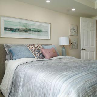 A cozy bedroom featuring a neatly made bed with various pillows and artwork above the headboard.