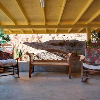 A cozy outdoor seating area featuring a wooden bench and rocking chairs, adorned with floral cushions, set against a decorative wall.