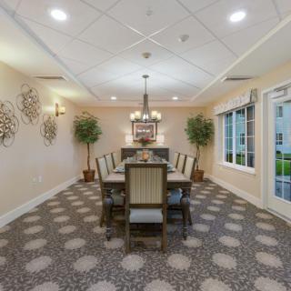 A well-lit dining room with a central chandelier, decorative walls, and large windows.