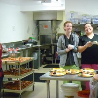 A group of people laughing and preparing food in a kitchen.