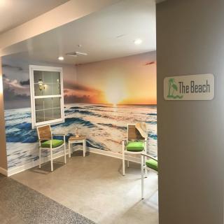 A cozy indoor seating area with chairs and a mural of a sunset over the ocean.