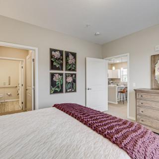 A cozy bedroom with a neatly made bed, artwork on the walls, and a dresser.