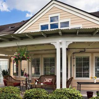 A cozy house with a covered porch and outdoor seating, surrounded by a lush garden.