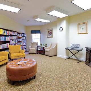 A cozy reading room with bookshelves, comfortable chairs, a round ottoman, and a piano keyboard.