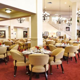A spacious and elegantly designed restaurant dining area with neatly arranged tables and chairs under ornate chandeliers.