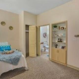 A cozy bedroom with a neatly made bed, decorative shelves, and an open doorway leading to a bathroom.