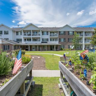 A scenic view of a residential building with gardens and flags under a partly cloudy sky.
