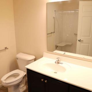 A clean and simple bathroom with a toilet, sink, mirror, and shower.