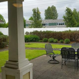A backyard view featuring a patio with outdoor furniture, a manicured lawn, and surrounding trees.
