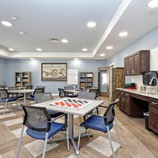 A spacious and modern community room equipped with tables, chairs, and a kitchenette.